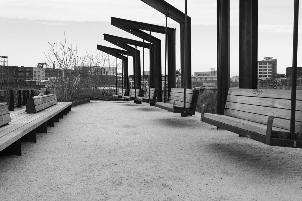 Black and white view of empty swing chairs and empty benches in Rail Line park.