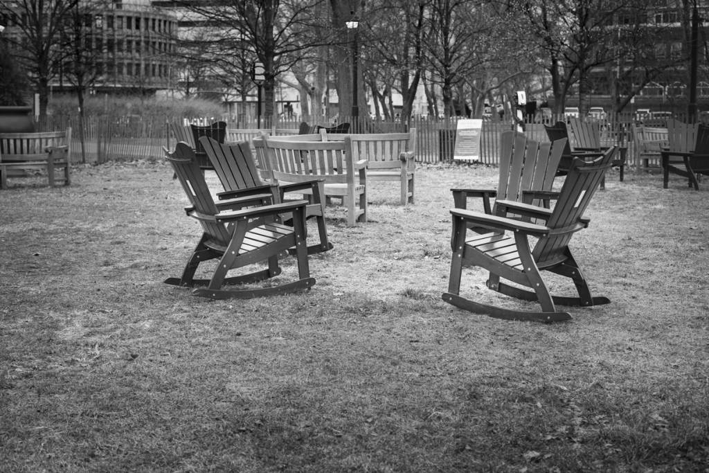 Black and white view of empty chairs and benches in park.