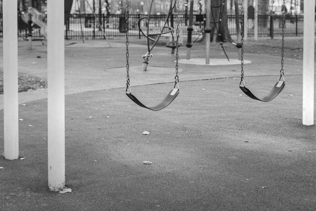 Black and white view of empty swings in playground.