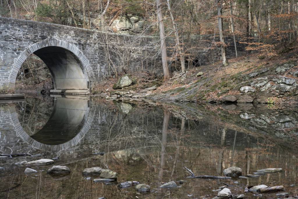 Color view of stone bridge mirrored in the Wissahickon Creek.